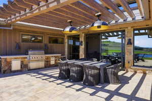 Outdoor patio featuring a built-in stainless steel grill, stone veneer base, and a wood pergola with integrated lighting