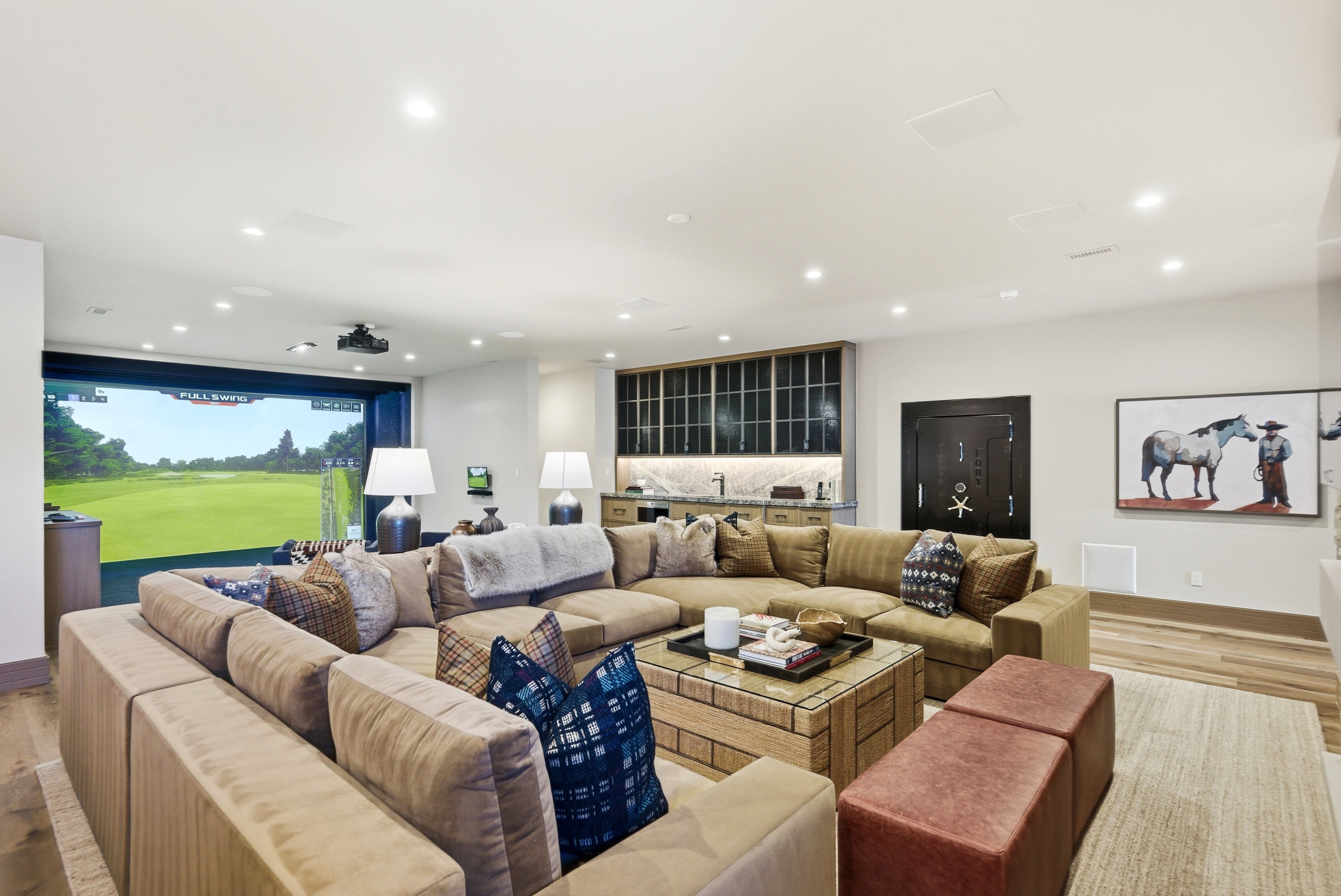 Dedicated entertainment room featuring a golf simulator, built-in wet bar with marble-finish countertop, wood-finish flooring, recessed lighting, and a dark-finish vault door