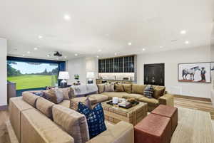 Dedicated entertainment room featuring a golf simulator, built-in wet bar with marble-finish countertop, wood-finish flooring, recessed lighting, and a dark-finish vault door