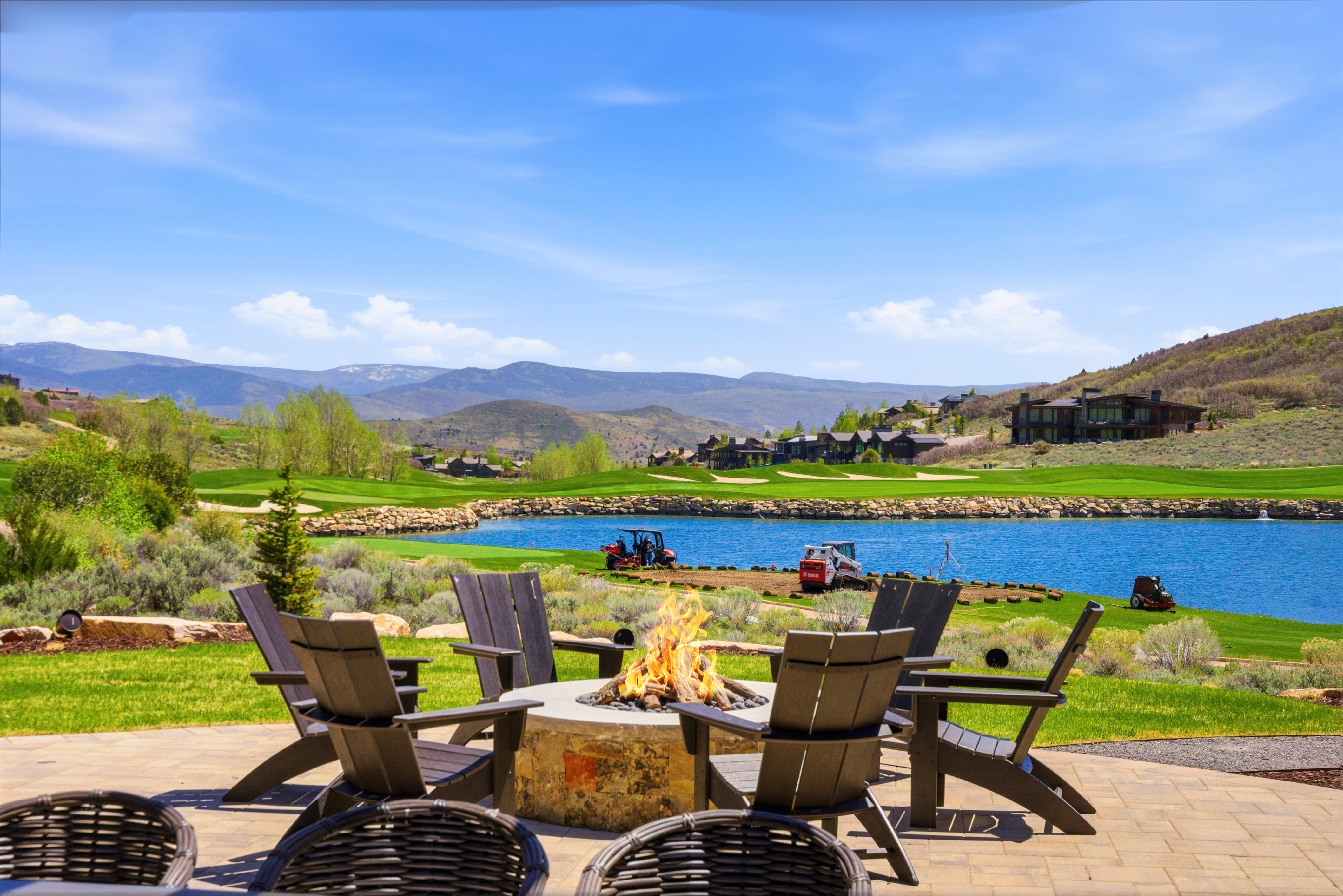 Expansive paver patio featuring a built-in stone fire pit, bordered by a manicured lawn