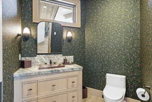 Powder room featuring a custom vanity with a stone countertop, a vessel sink, and a framed mirror