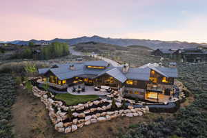 Expansive mountain modern residence featuring a dark wood and stone exterior, a multi-tiered metal roofline, and extensive window walls