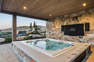 Covered patio area featuring a built-in hot tub with integrated lighting, wood-finish ceiling, and a stone accent wall