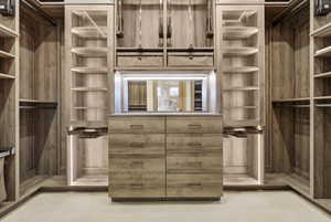 Built-in closet system featuring wood-finish cabinetry, central dresser with integrated drawers, glass-front display cabinets, pull-out hanging rods, and integrated LED lighting