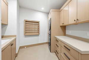Dedicated laundry room featuring extensive light wood-finish cabinetry with dark hardware, solid surface countertops, and an integrated drying rack
