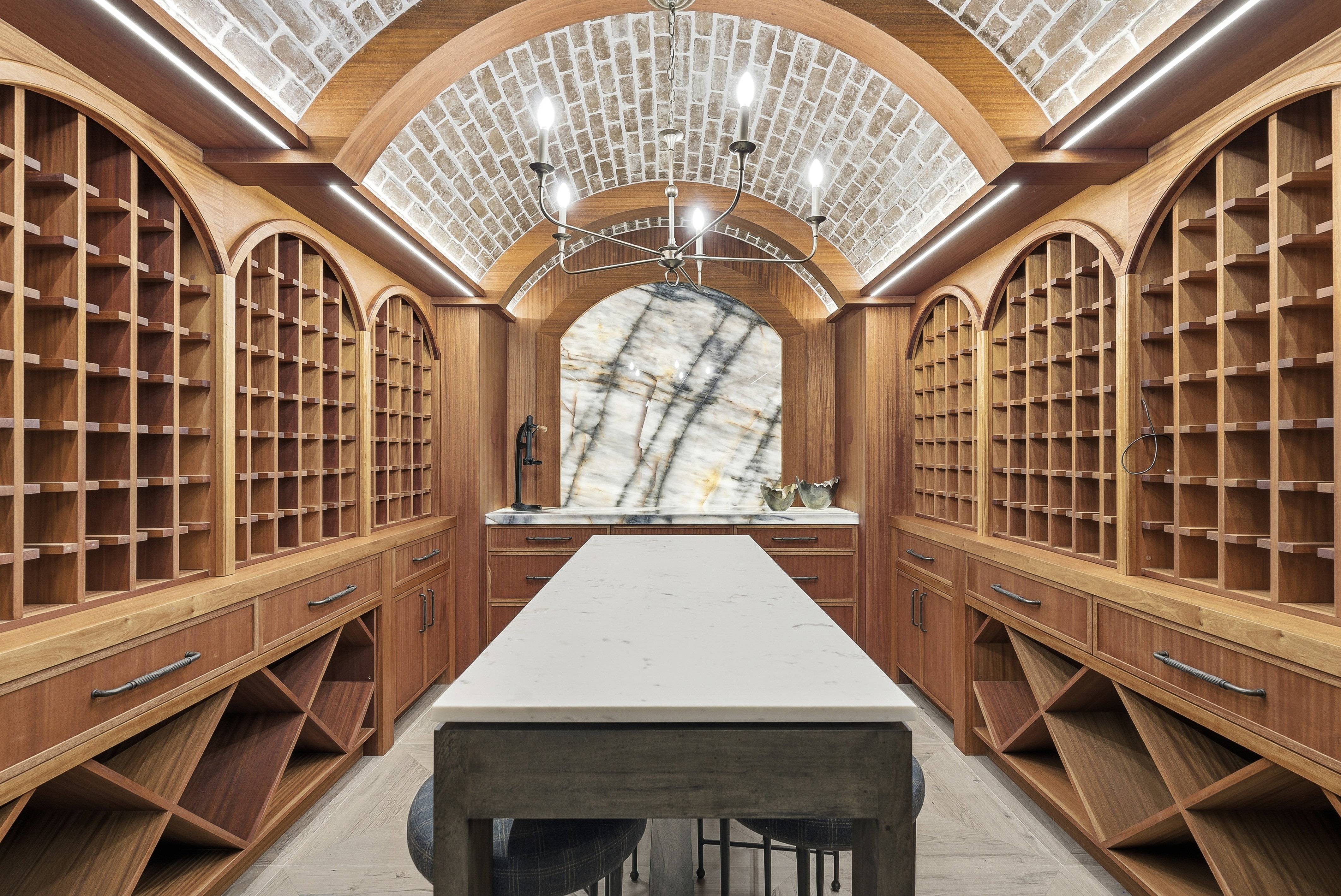 Custom wood-finish wine cellar featuring arched brick ceiling, integrated lighting, a central stone-top island, and a natural stone accent wall