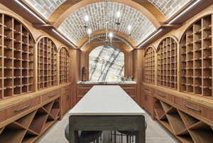 Custom wood-finish wine cellar featuring arched brick ceiling, integrated lighting, a central stone-top island, and a natural stone accent wall