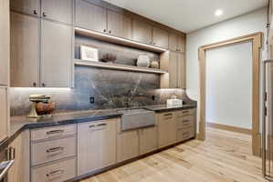 Custom cabinetry with integrated under-cabinet lighting, a deep farmhouse-style sink, and a dark stone countertop with a matching backsplash