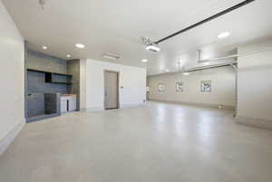 Spacious garage featuring a tiled utility sink area with built-in shelving, light-colored concrete flooring, recessed ceiling lighting, and an automatic garage door opener