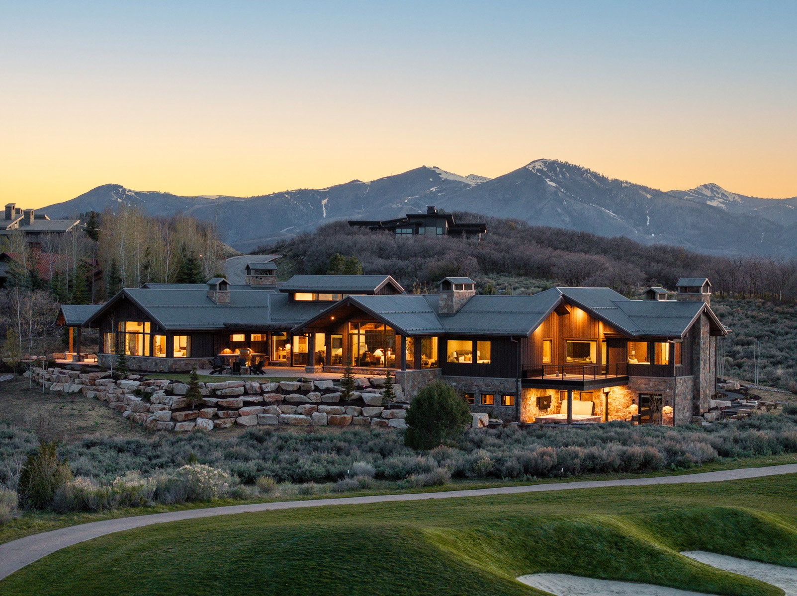 Expansive property featuring a stone and wood facade, multiple levels of outdoor living space, and a golf course frontage