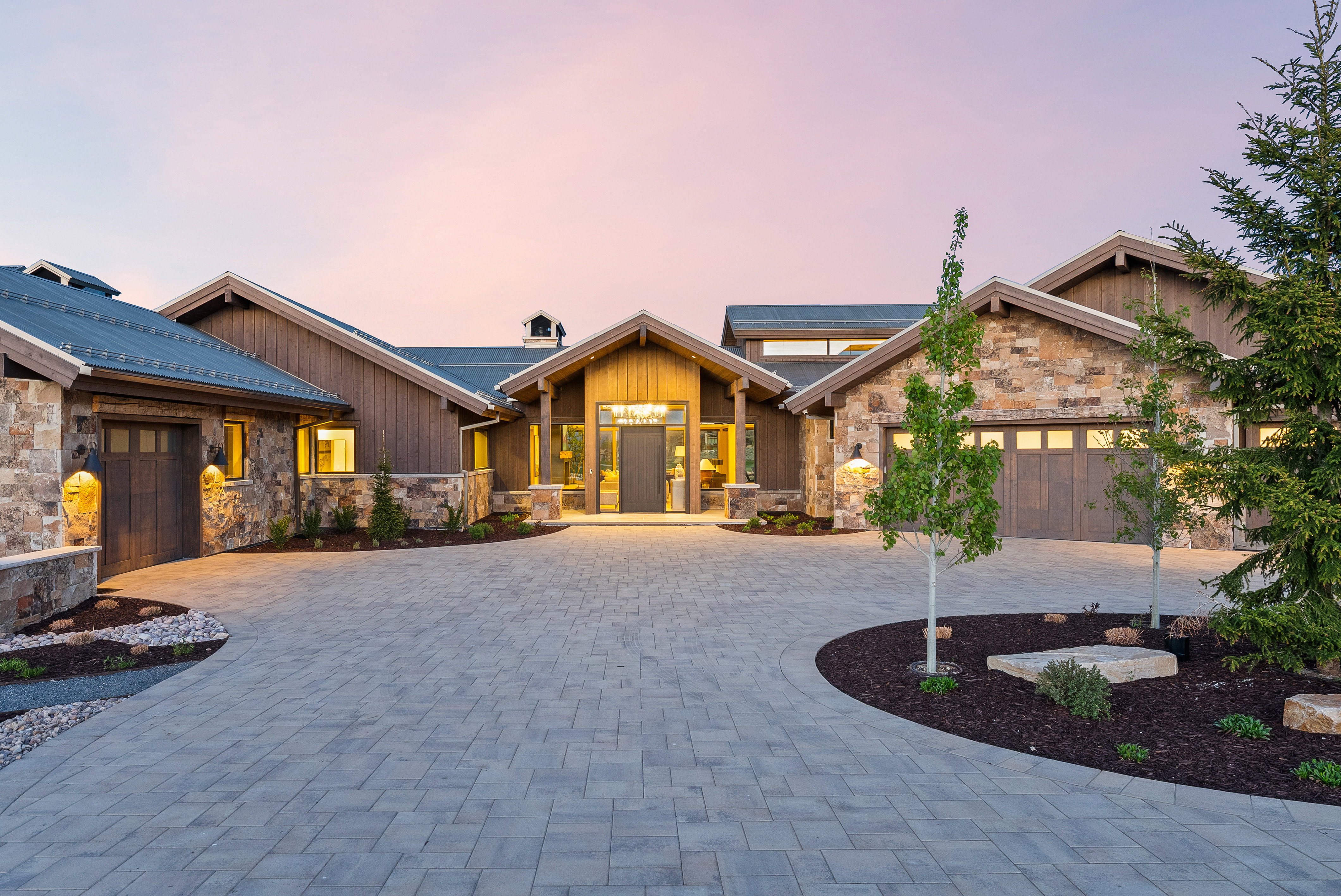 Stone and wood-sided exterior featuring a paver driveway, multiple garage doors, and a covered entry