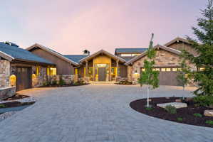 Stone and wood-sided exterior featuring a paver driveway, multiple garage doors, and a covered entry