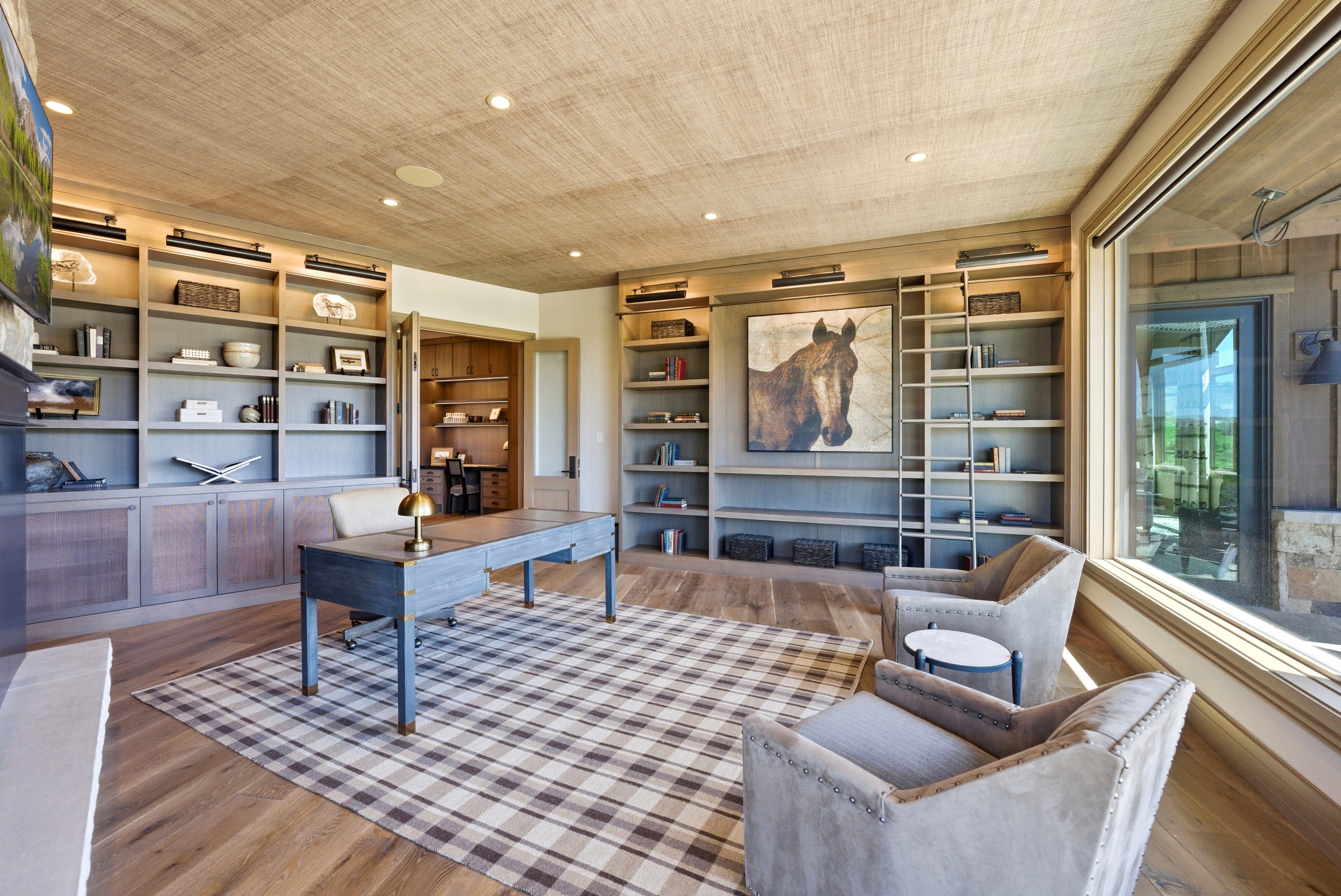 Wood-finish flooring anchors this space featuring extensive built-in shelving, a full-height rolling ladder, and a grasscloth ceiling