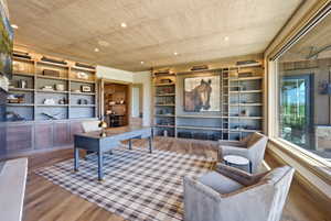 Wood-finish flooring anchors this space featuring extensive built-in shelving, a full-height rolling ladder, and a grasscloth ceiling