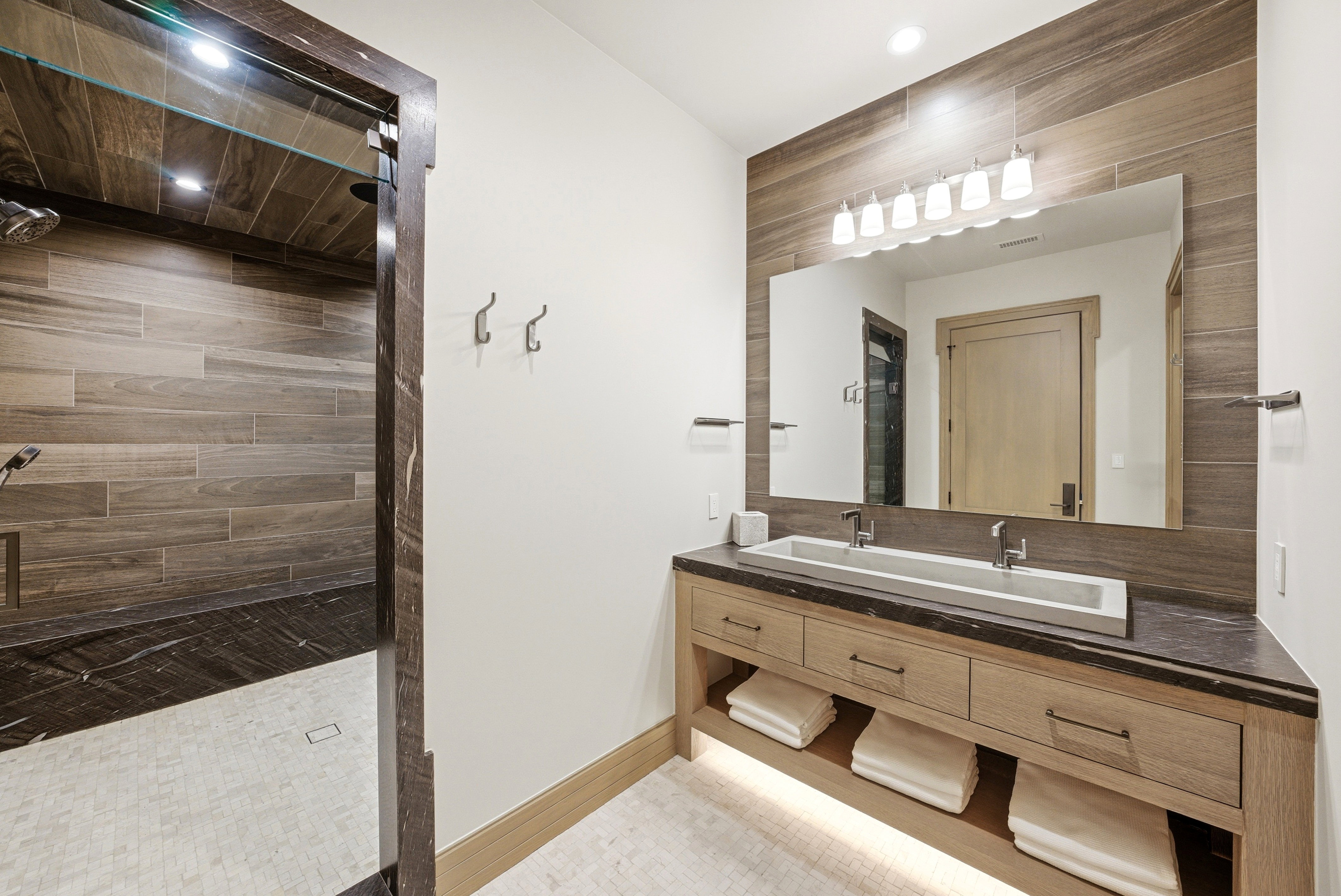Wood-finish tile shower with a dark stone bench and light tile flooring