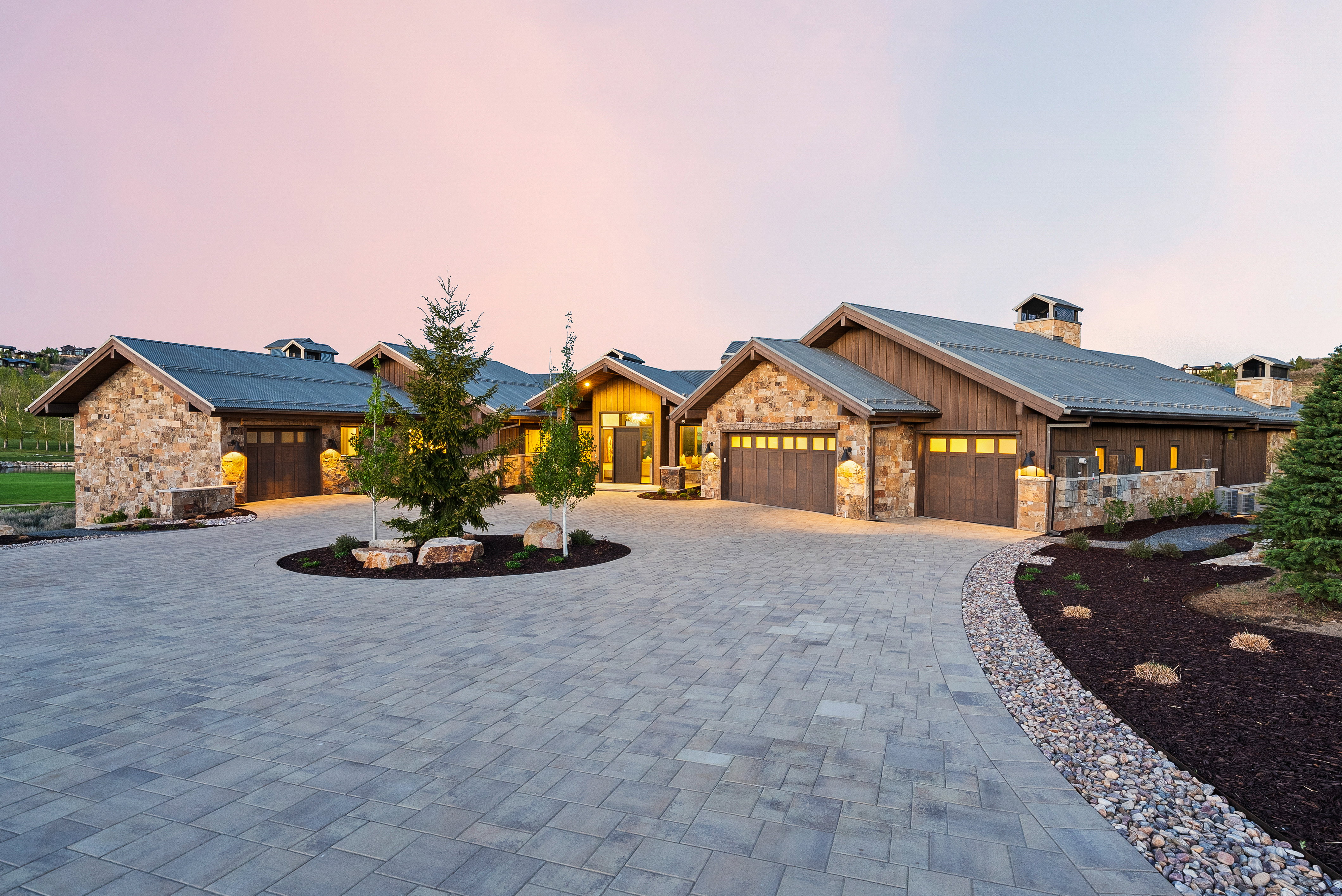 Stone and wood-sided exterior featuring multiple garage bays and a paver driveway
