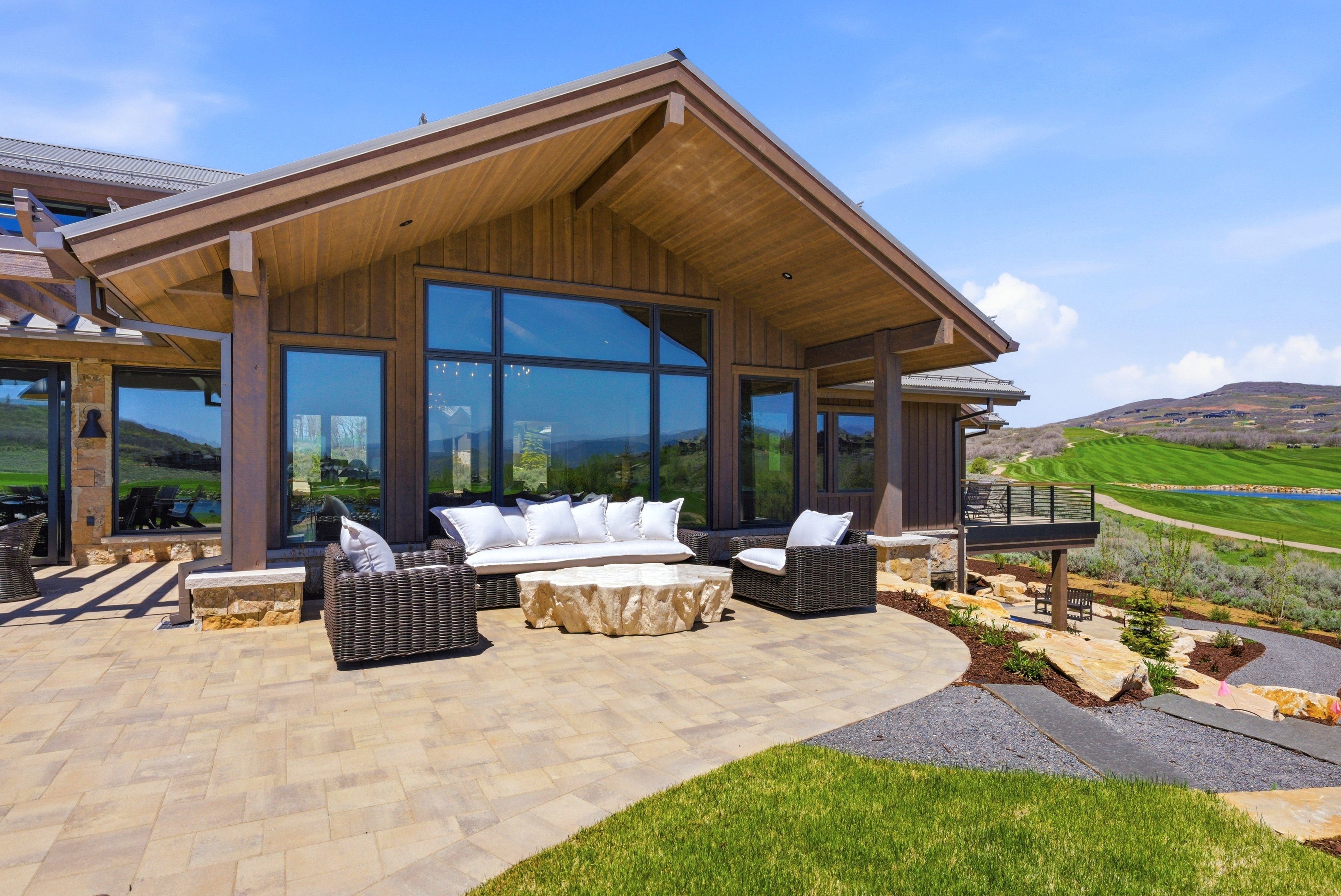Expansive outdoor patio featuring a large paver surface, stone accent walls, and a wood-paneled ceiling