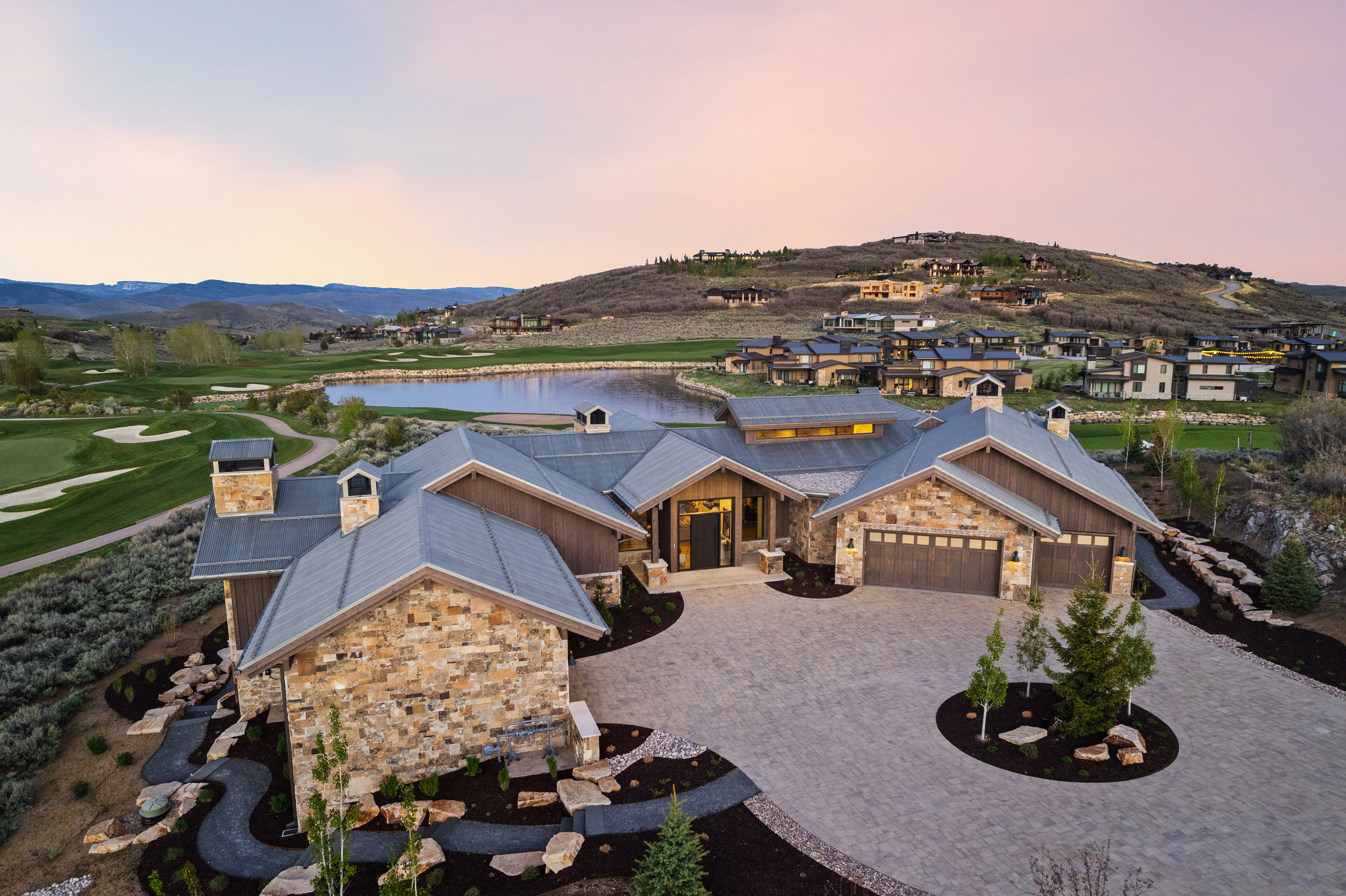 Stone and wood-sided exterior featuring multiple gables, a paver driveway, and a two-car garage