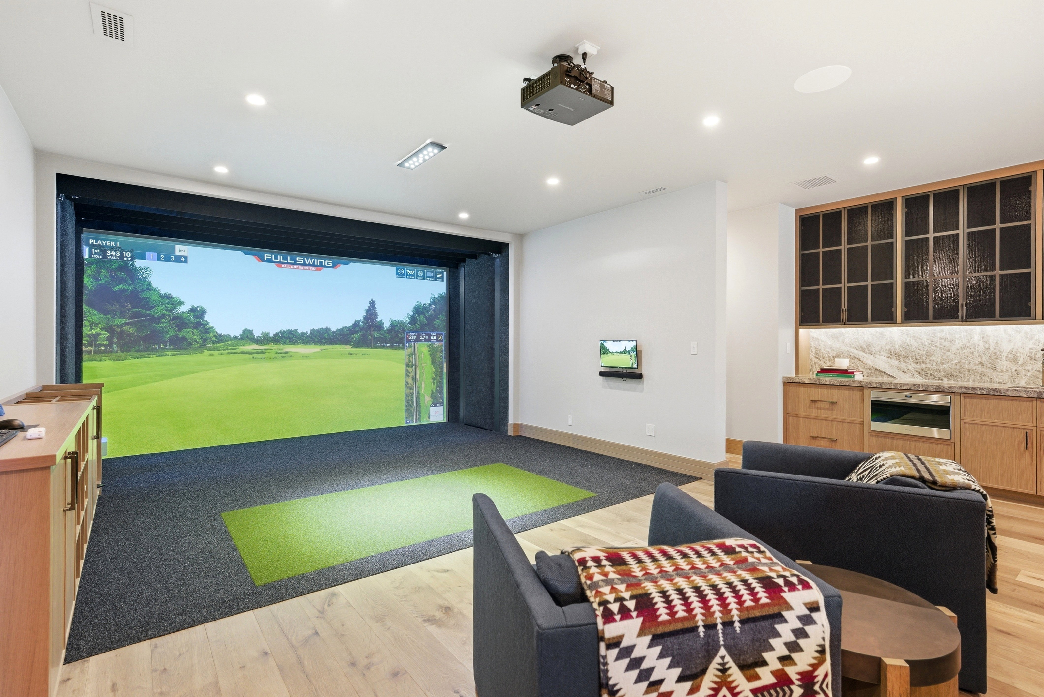 Dedicated golf simulation room featuring a large projector screen, integrated projector, and recessed ceiling lighting