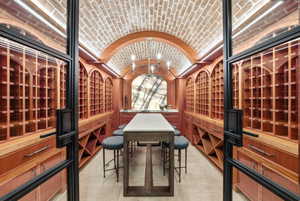 Custom wine cellar featuring an arched brick ceiling, extensive wood-finish cabinetry, built-in wine racks, an illuminated stone accent wall, and a central tasting table
