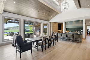 Open-concept living space featuring wood-finish flooring, a vaulted wood-paneled ceiling with exposed beams, and a dining area with direct patio access