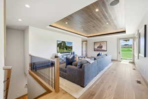 Spacious living area featuring light wood-finish flooring, a contemporary ceiling with recessed lighting, and a door opening to a vibrant green outdoor space
