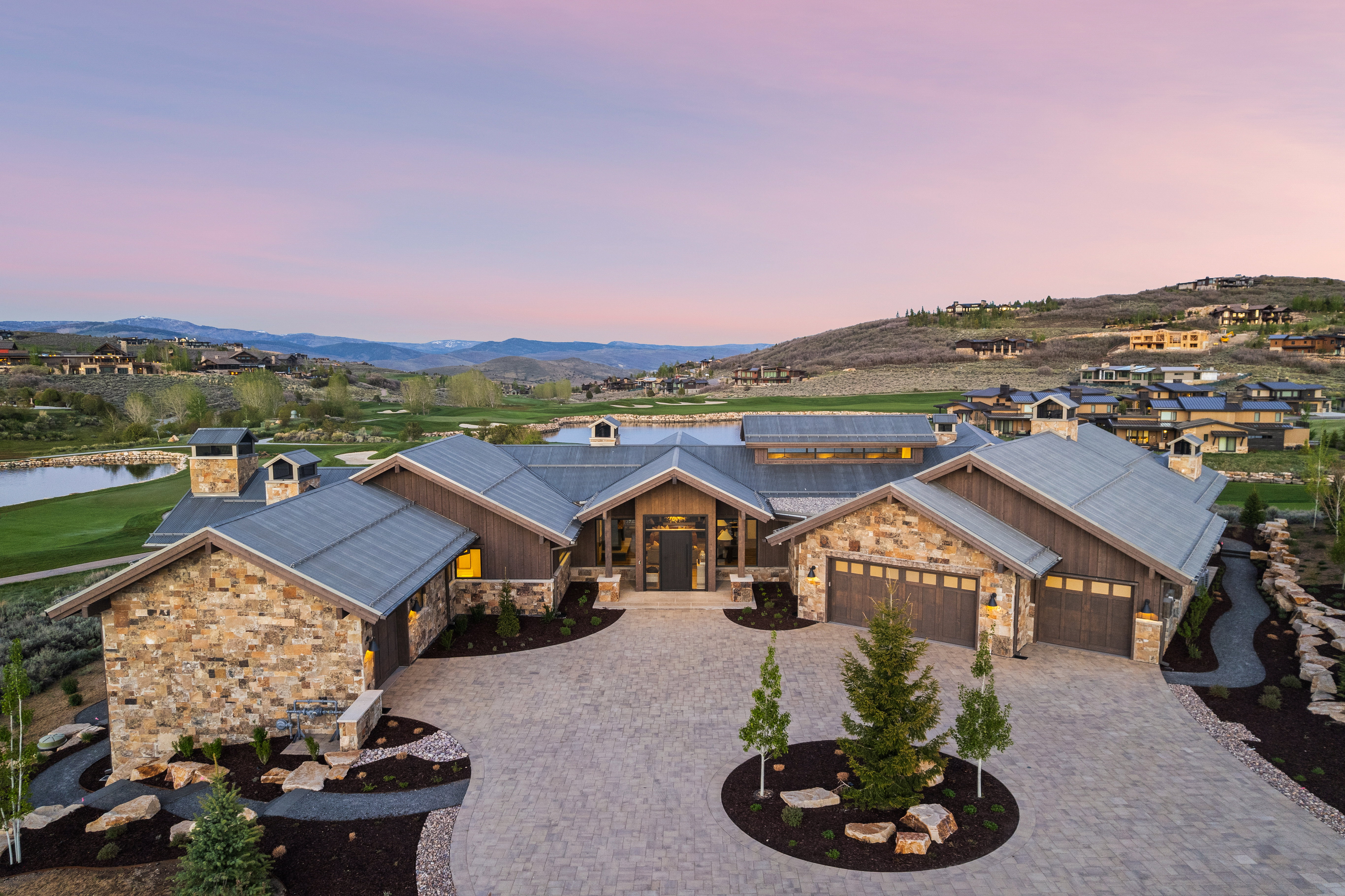 Expansive stone and wood-clad exterior with a multi-car garage, large driveway, and landscaped grounds