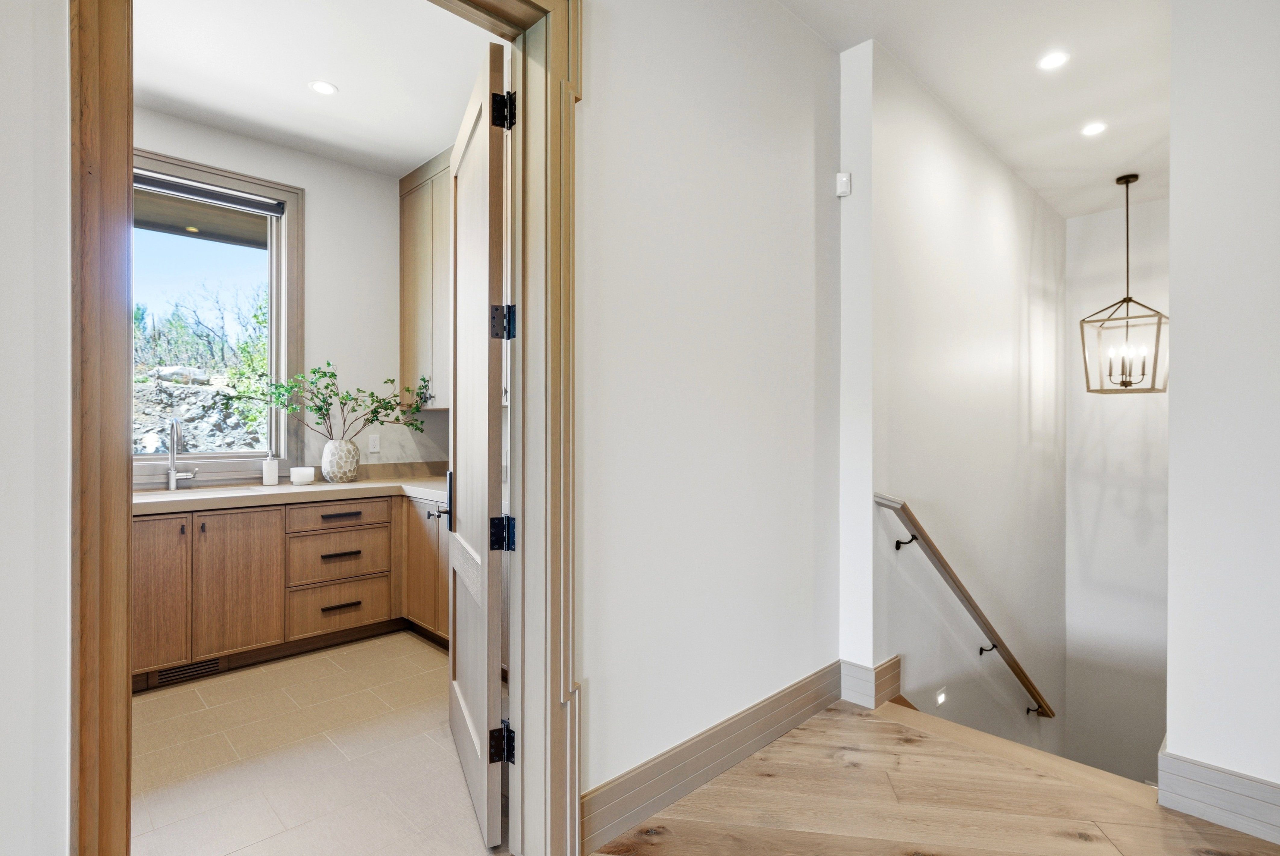 Warm wood-finish flooring and baseboards define this hallway, featuring a staircase with a wood handrail