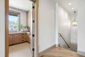 Warm wood-finish flooring and baseboards define this hallway, featuring a staircase with a wood handrail
