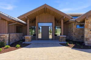Grand entrance featuring a double door with sidelights, timber frame porch, natural stone veneer, vertical wood siding, and a paver driveway