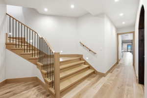 Light wood-finish flooring extending into a hallway with recessed lighting