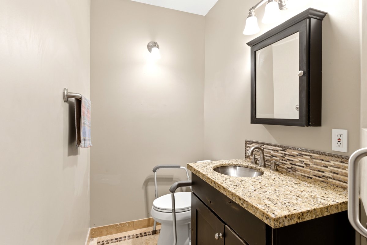Bathroom vanity featuring a granite countertop, stainless steel sink, dark wood cabinetry, and a mosaic tile backsplash