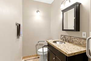 Bathroom vanity featuring a granite countertop, stainless steel sink, dark wood cabinetry, and a mosaic tile backsplash