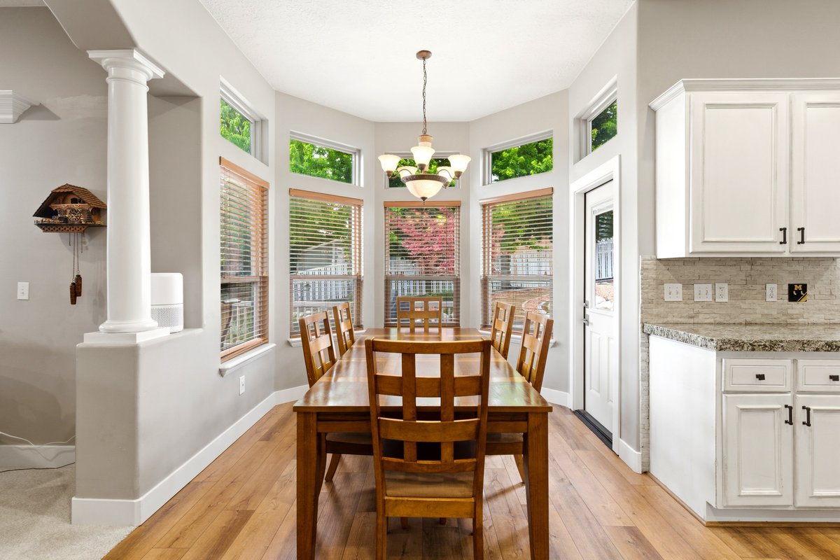 Bay window dining area with wood-finish flooring, featuring a chandelier and multiple windows with wood blinds