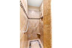Walk-in shower featuring natural stone-look wall tiles, pebble-detail accent bands, a built-in shower bench, and a brushed nickel grab bar