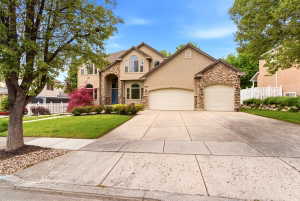 Stucco and stone facade with arched entry, complementing double garage doors, a large paved driveway, and mature landscaping