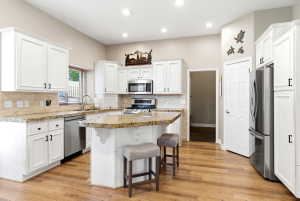 Kitchen featuring white cabinetry, granite countertops, stainless steel appliances, a breakfast bar, and wood-finish flooring