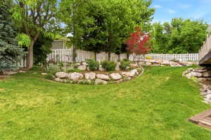 Expansive backyard featuring a lush lawn, mature trees, and a white picket fence
