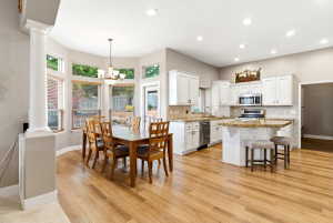 Open-concept kitchen and dining area featuring light wood-finish flooring, white cabinetry, and granite countertops