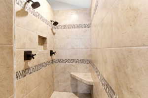 Tiled shower featuring dual shower heads, a built-in niche, a corner bench, and decorative mosaic tile accents