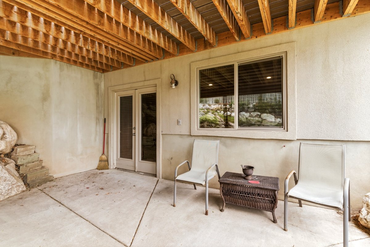 Concrete patio area featuring a textured stucco exterior, exposed wood joists, and a glass sliding door