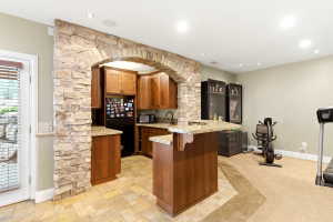 Stone archway defining a kitchen area featuring wood cabinetry, granite countertops, and tile flooring