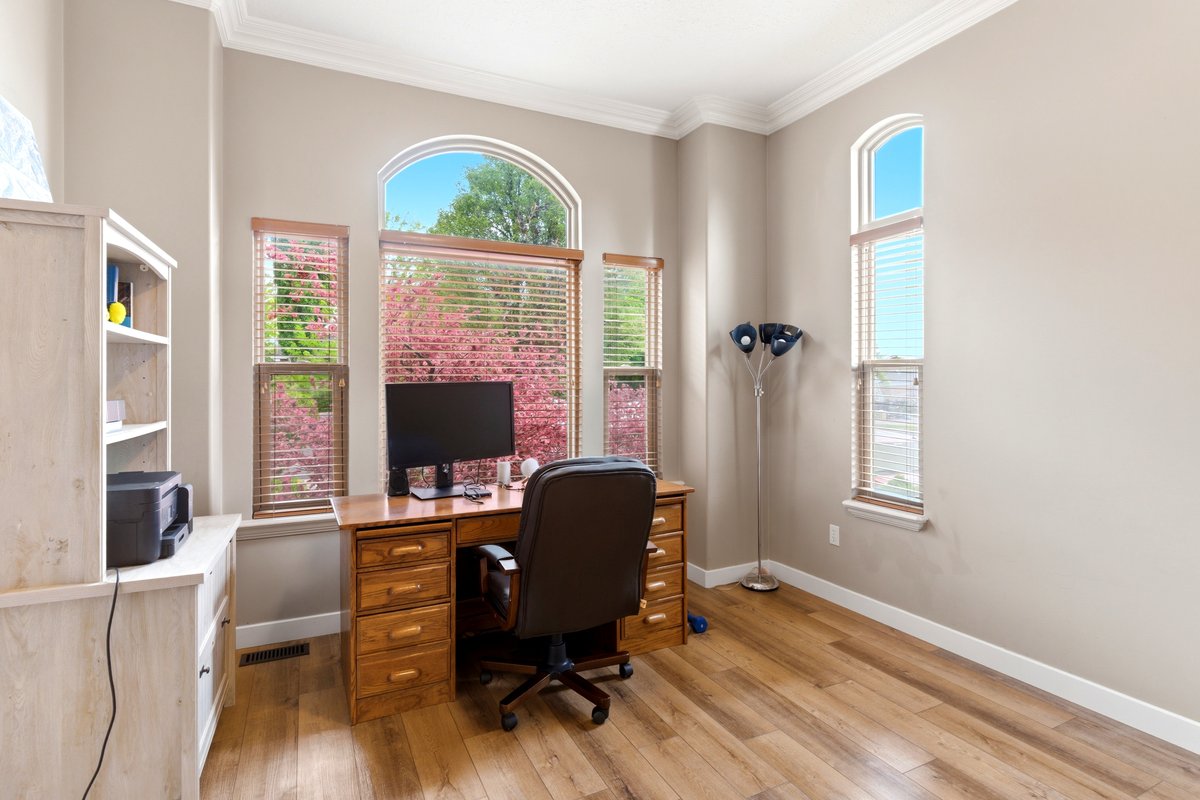 Bright room featuring wood-finish flooring, tall ceilings with crown molding, and multiple windows with arched transom details