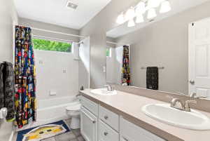 Bathroom featuring a double vanity with integrated sinks, a tub/shower combination with white tile surround, and a horizontal window providing natural illumination