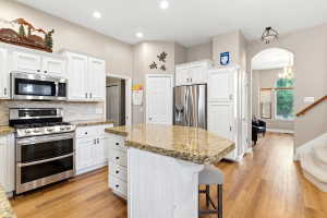 Kitchen featuring white cabinetry, stainless steel appliances, speckled countertops, a tile backsplash, and wood-finish flooring