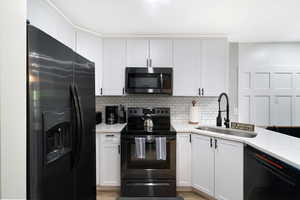 Contemporary kitchen featuring white cabinetry, black hardware, black appliance suite, subway tile backsplash, and light-toned countertops
