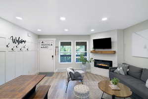 Open-concept living area with wood-finish flooring, recessed lighting, and a corner electric fireplace with a wood mantel