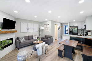 Open-concept living space featuring wood-finish flooring, recessed lighting, and a modern fireplace with a wood mantle