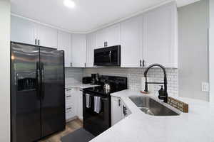 Contemporary kitchen featuring white shaker cabinetry, light-toned countertops, a subway tile backsplash, and a stainless steel sink with a matte black pull-down faucet