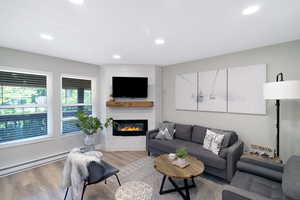 Living area featuring an electric fireplace with a wood mantle and shiplap-style surround, recessed ceiling lights, wood-finish flooring, and multiple windows with blinds